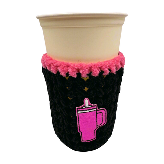 A crocheted cozy in black with purple trim, displayed around a cup, against a white background.