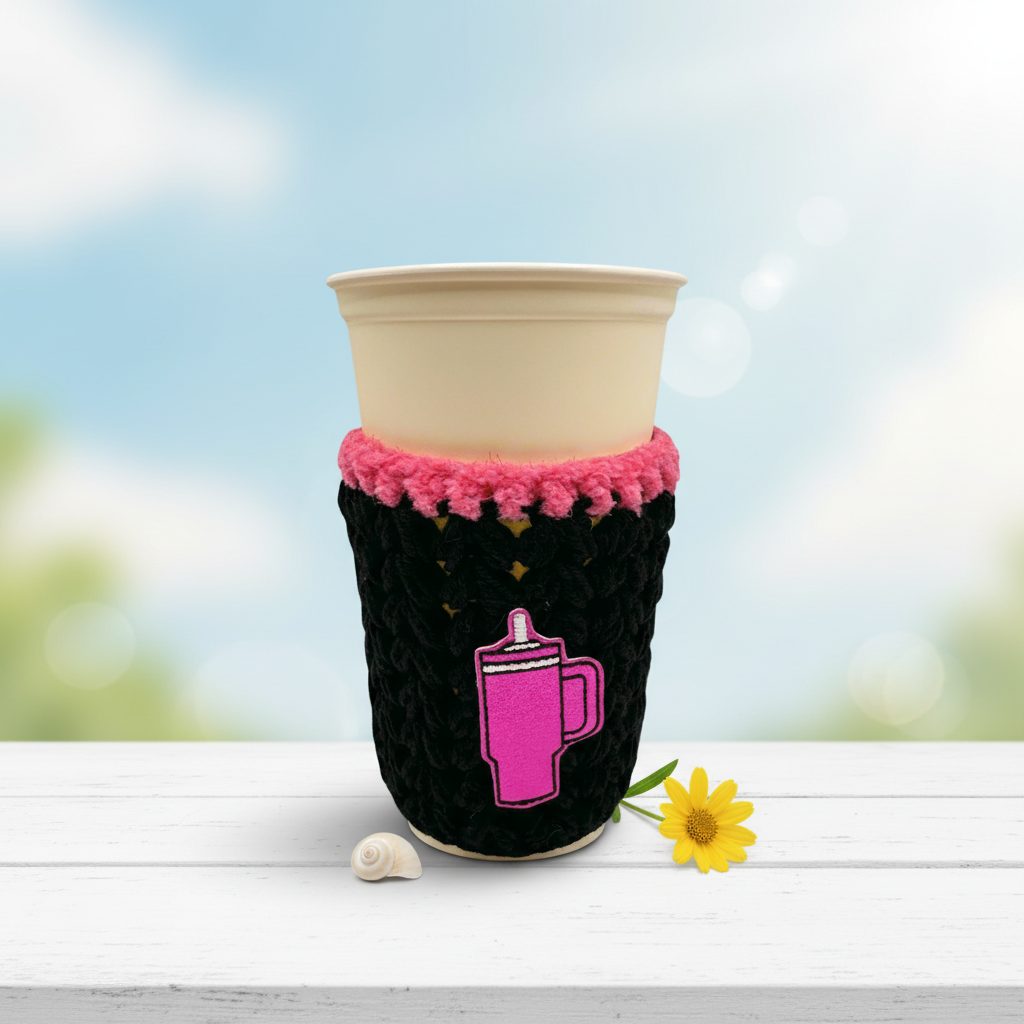 A crocheted cozy in black with purple trim, displayed around a cup, against a white background.