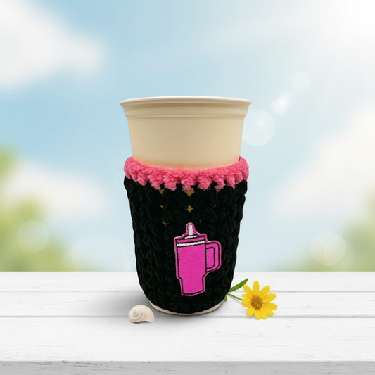 A crocheted cozy in black with purple trim, displayed around a cup, against a white background.