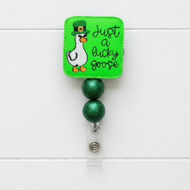 Retractable badge holder with a cartoon goose and text 'Just a lucky goose' on a green background.