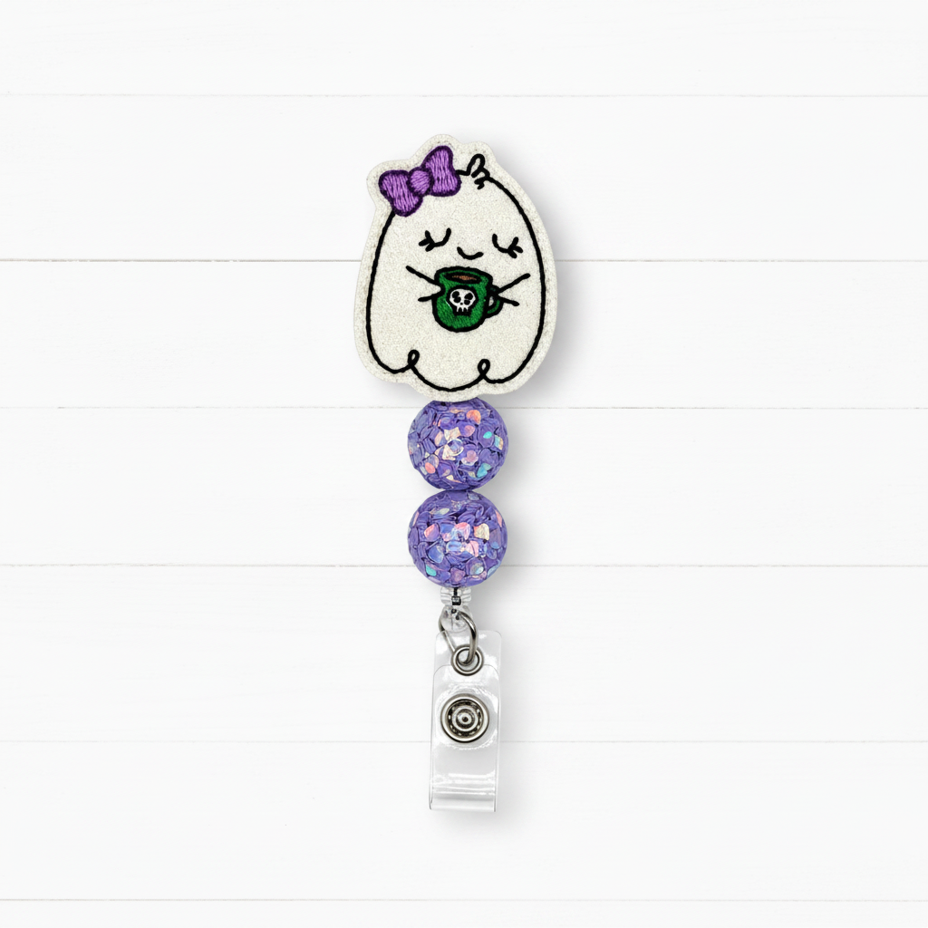 A ghost-themed retractable badge reel featuring a white embroidered ghost with a purple bow and green mug, accented with two purple glitter beads and a clear plastic clip.