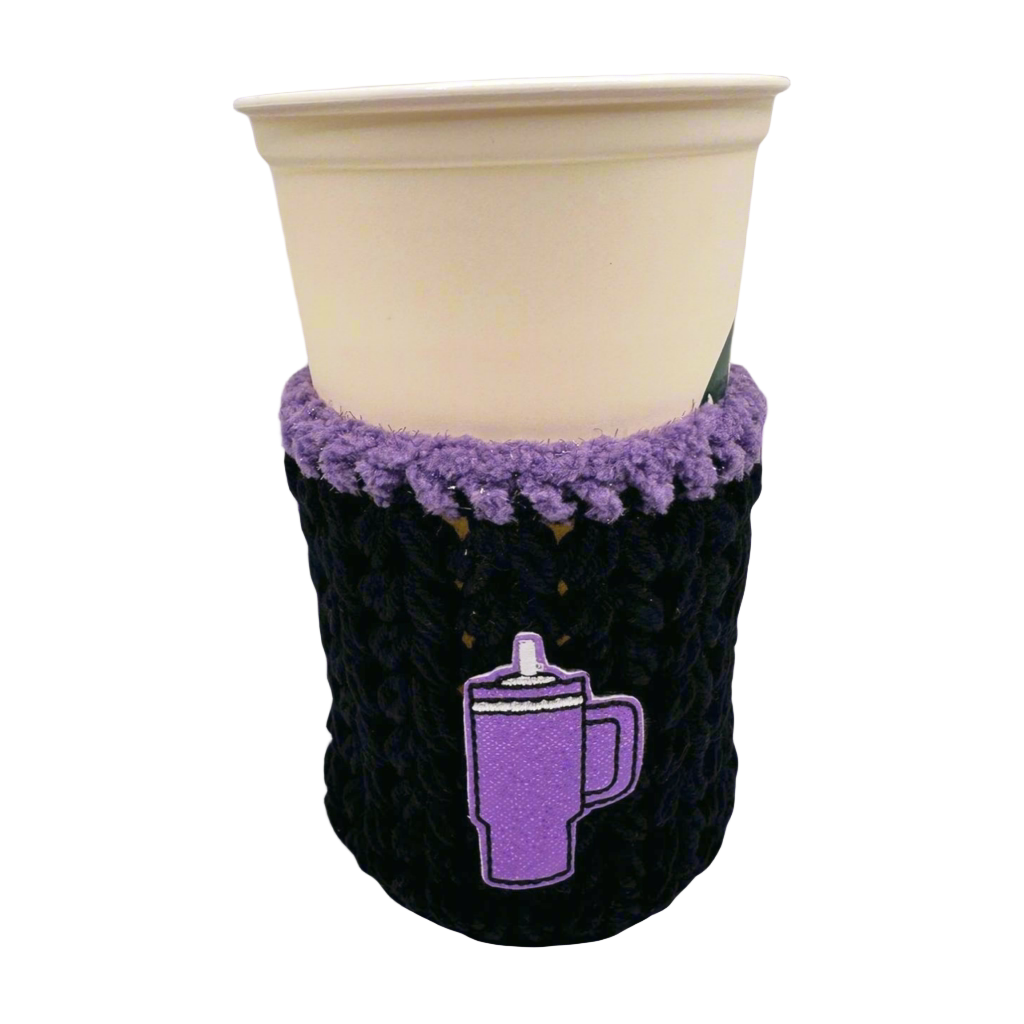 A crocheted cozy in black with purple trim, displayed around a cup, against a white background.