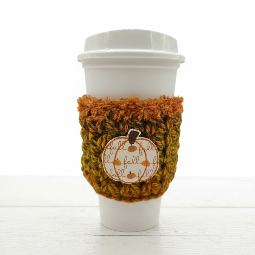 Coffee cup with a cozy fall-themed sleeve on a wooden surface.