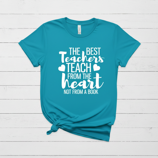Blue t-shirt with 'The Best Teachers Teach from the Heart Not from a Book' text on a wooden surface with school supplies.