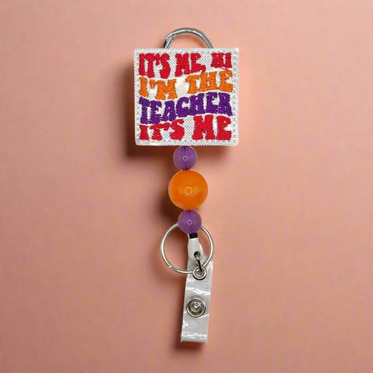 A badge reel with a colorful reel cap featuring text and decorative elements, attached to a clip and a retractable cord, displayed against a pink background.