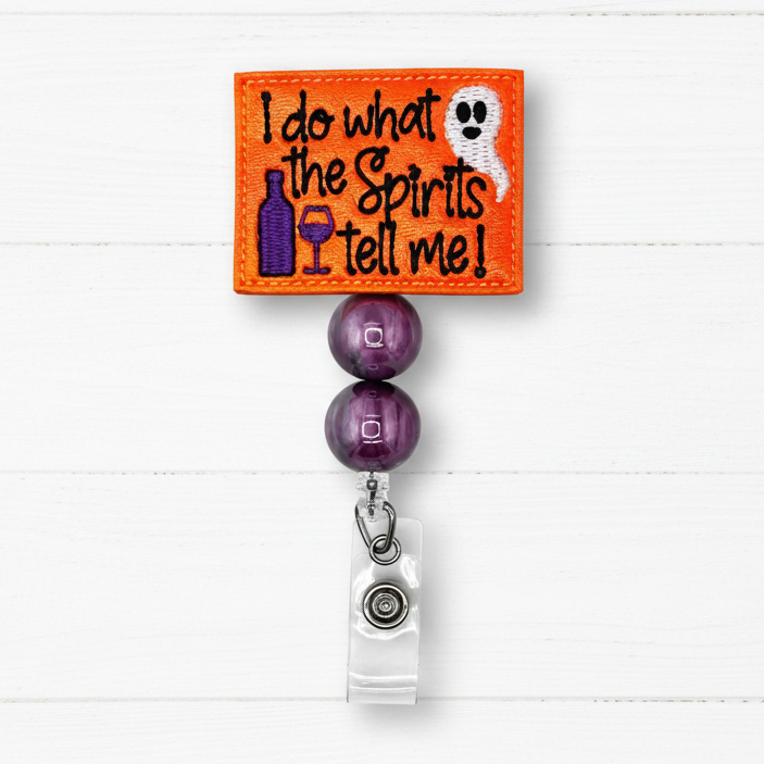 An embroidered Halloween-themed bistro rod clip. The bright orange square patch features the text 'I do what the Spirits Tell Me!' in black, alongside a purple bottle, a purple wine glass, and a white ghost.