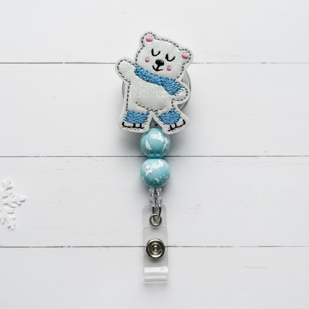 Polar bear-themed badge holder with blue beads on a white wooden background with snowflakes and greenery.