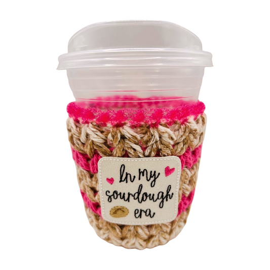 Coffee cup with pink and beige woven sleeve and 'In my sourdough era' patch on a white background