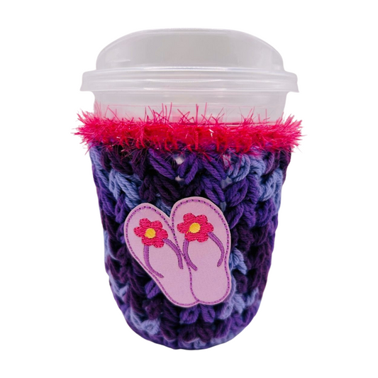Coffee cup with a purple and pink crochet sleeve featuring flip-flop design on a white background