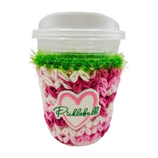 Coffee cup with a pink and green textured sleeve and 'Pickleball' heart logo on a white background