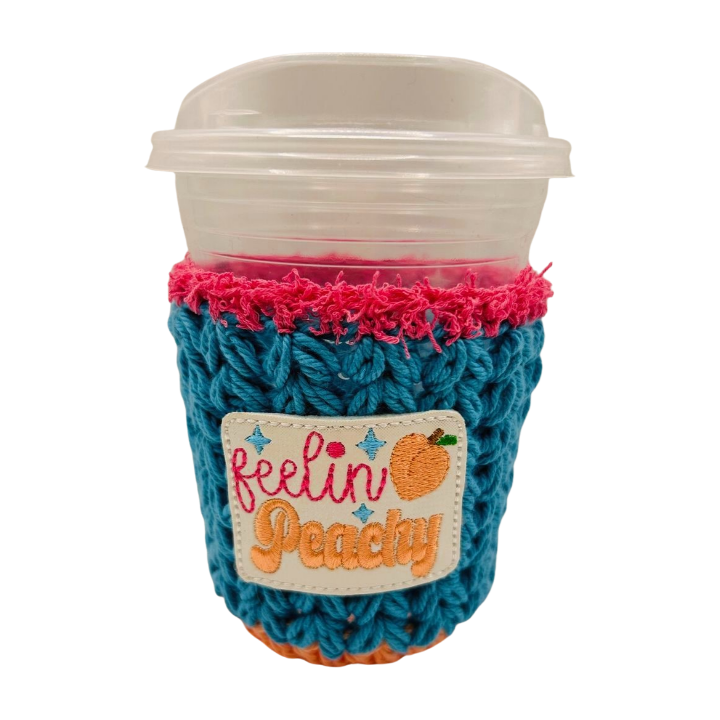 Coffee cup with a blue knitted cozy and pink rim, featuring 'feelin' peachy' text.