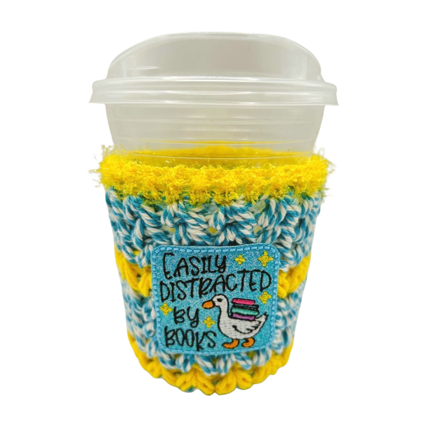 Coffee cup with a yellow and blue knit cozy featuring text and a duck illustration.