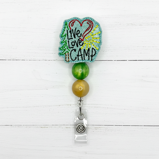 A badge reel with a multicolored design, featuring the text 'LIVE LOVE CAMP' on a heart-shaped background, attached to a clip.
