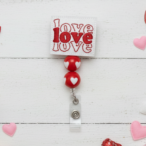 Red and white badge holder with 'love' text on a light wooden surface.