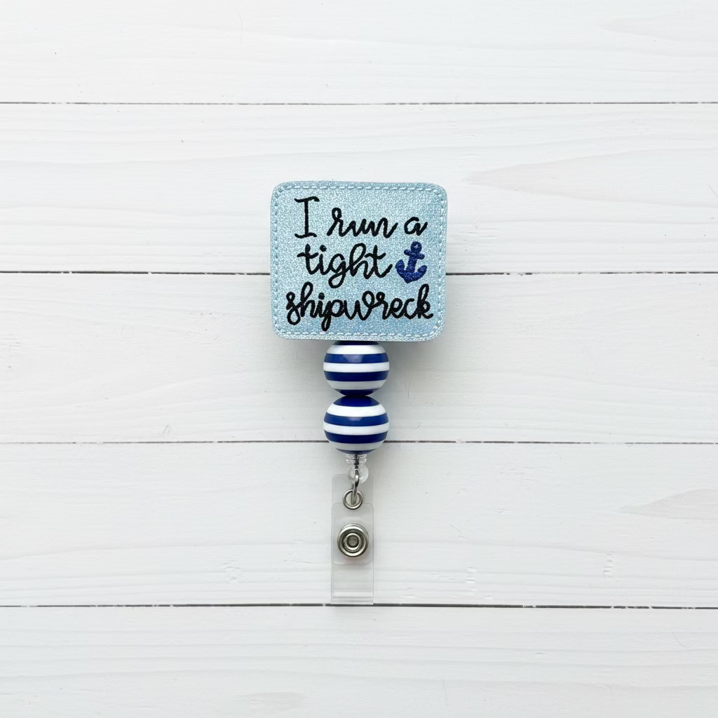 A nautical-themed retractable badge reel with a square blue plaque that reads 'I run a tight shipwreck' in black script with a blue anchor graphic. The plaque and striped rod are decorated in light blue and dark blue, and the badge is held by a silver clasp on a clear plastic sleeve, set against a light pink background.