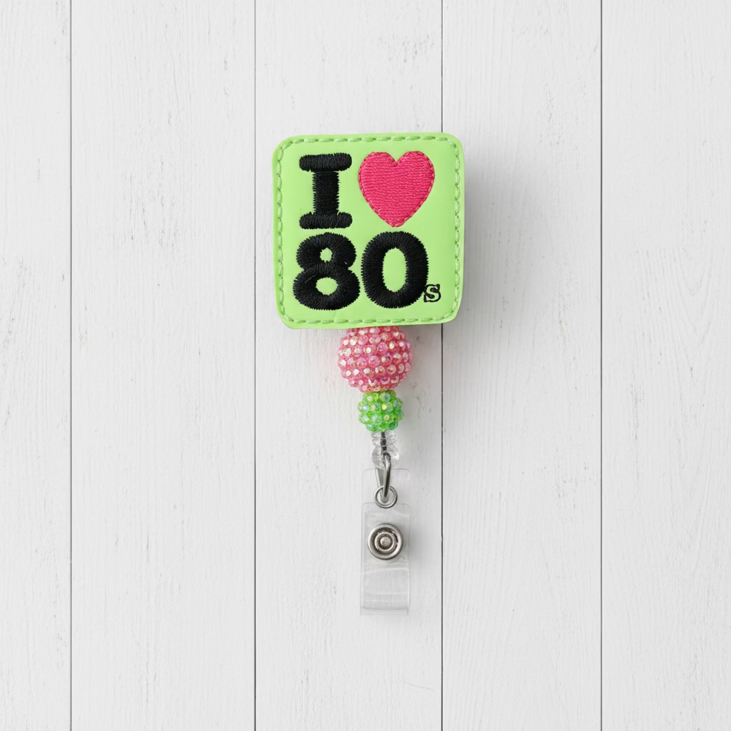 A square embroidered badge reel featuring a bright lime green background with 'I' and '80' in black, a pink heart, and a beaded pink and green loop with a silver clip.