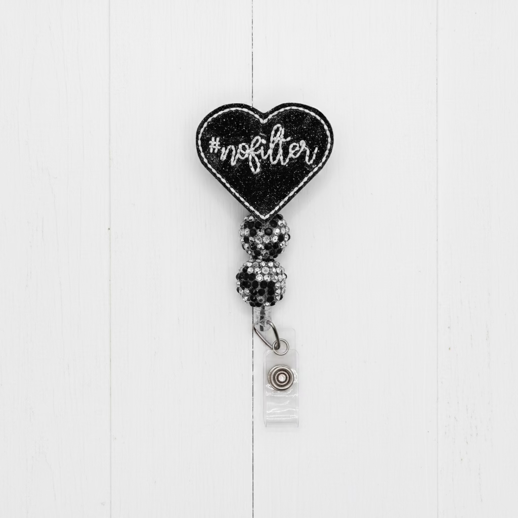 A black glitter heart-shaped badge reel with the word 'nofilter' in white script, attached to a clear plastic snap hook with a silver metal ring, set against a plain light pink background.