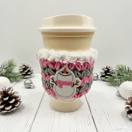 A coffee cozy sleeve with a snowman design, primarily in blue and gray tones, wrapped around a coffee cup.