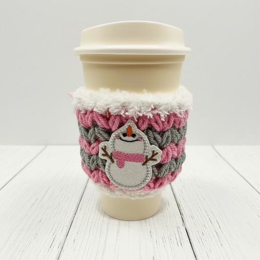 A coffee cozy sleeve with a snowman design, primarily in blue and gray tones, wrapped around a coffee cup.