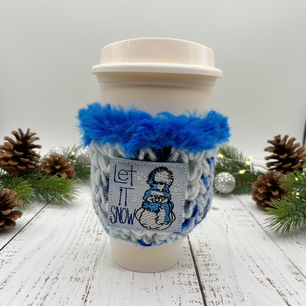 A coffee cozy with blue and white colors, featuring a snowman design and the text 'Let it snow'.