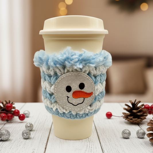 Crocheted snowman coffee cozy on a cup with Christmas decorations in the background