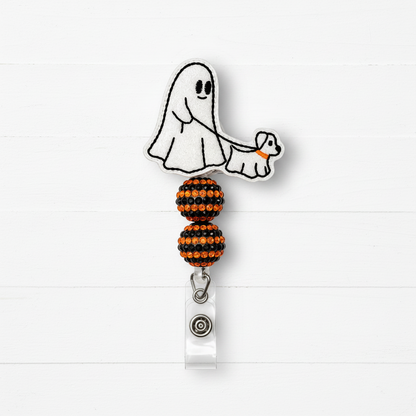 A Halloween-themed retractable badge reel featuring a white embroidered ghost and dog design with orange accents, attached to a clear plastic clip with a silver snap button, set against a white wood plank background.