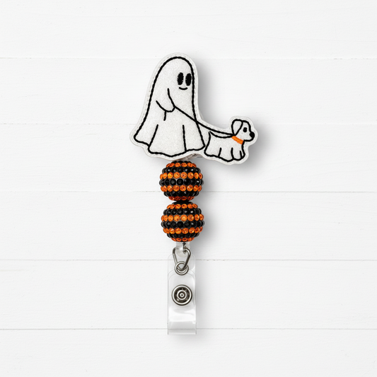 A Halloween-themed retractable badge reel featuring a white embroidered ghost and dog design with orange accents, attached to a clear plastic clip with a silver snap button, set against a white wood plank background.