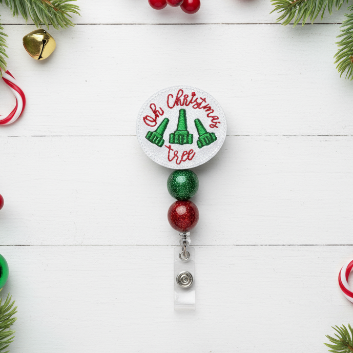 Christmas-themed badge holder with green and red beads on a white wooden background with holiday decorations.