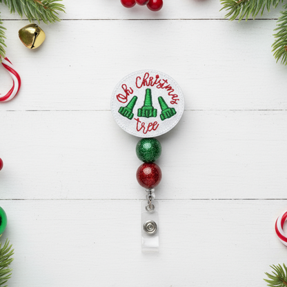 Christmas-themed badge holder with green and red beads on a white wooden background with holiday decorations.