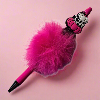 A pink pen with a decorative pumpkin charm and beads, attached to a fluffy pink top.