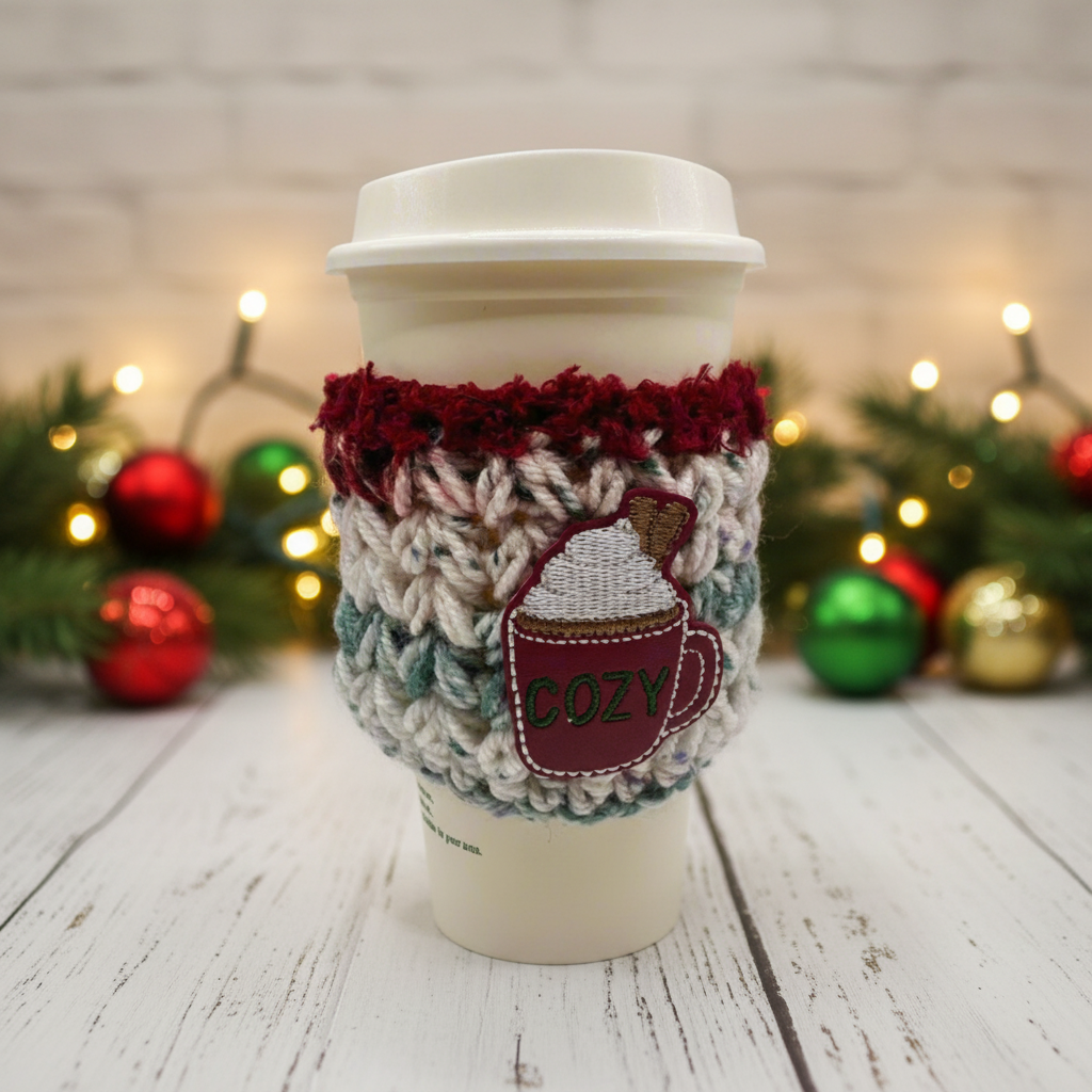 Coffee cup with a cozy sleeve featuring a hot chocolate design and 'COZY' text, set against a festive background with Christmas decorations.