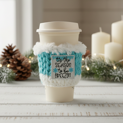 Coffee cup with turquoise and white cozy and decorative sign, surrounded by Christmas decor.