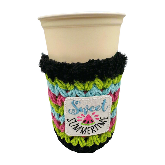 A crocheted multicolored drink cozy with the text 'Sweet Summertime' displayed on a cup.