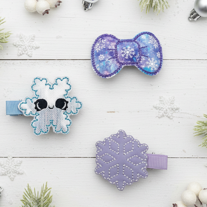 Three decorative hair clips with snowflake designs on a white wooden surface.