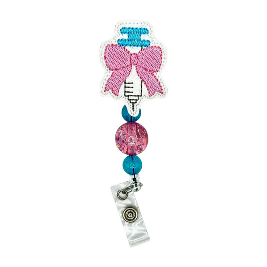Decorative badge holder with pink bow, blue beads, and clear clip on a white background