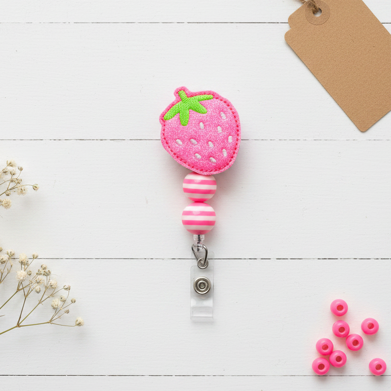 Pink strawberry-shaped badge holder on a white wooden surface with small pink beads and a tag.