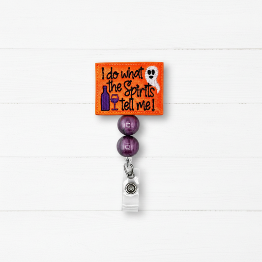 An embroidered Halloween-themed bistro rod clip. The bright orange square patch features the text 'I do what the Spirits Tell Me!' in black, alongside a purple bottle, a purple wine glass, and a white ghost.