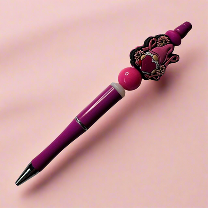 A purple pen with a beaded barrel featuring a pink ribbon and a small gnome design.