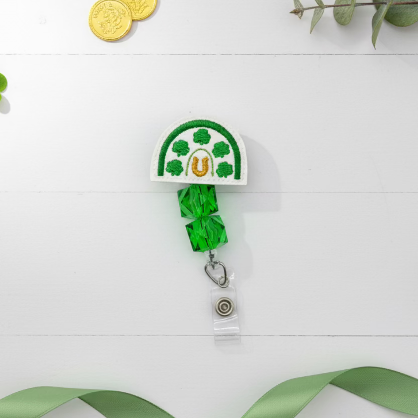 Decorative badge holder with shamrocks, a horseshoe, and green beads on a white background