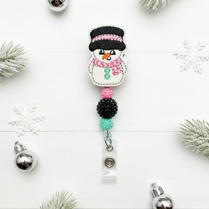 Snowman-themed badge holder with decorative beads on a white background with Christmas decorations.