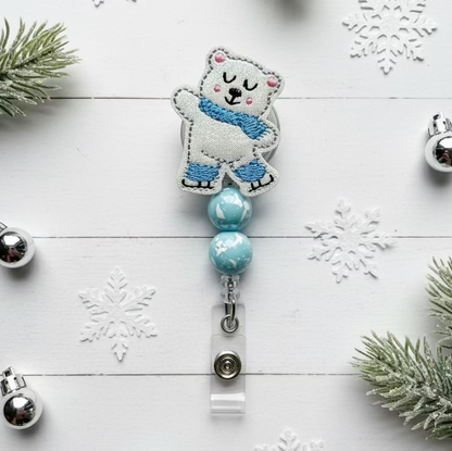 Polar bear-themed badge holder with blue beads on a white wooden background with snowflakes and greenery.