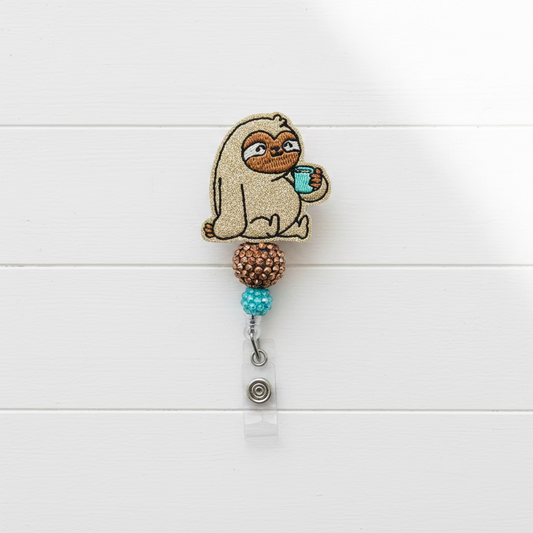 A custom embroidered brooch featuring a glittery gold sloth holding a teal cup, attached to a retractable badge reel with brown and teal beads, on a plain white background.