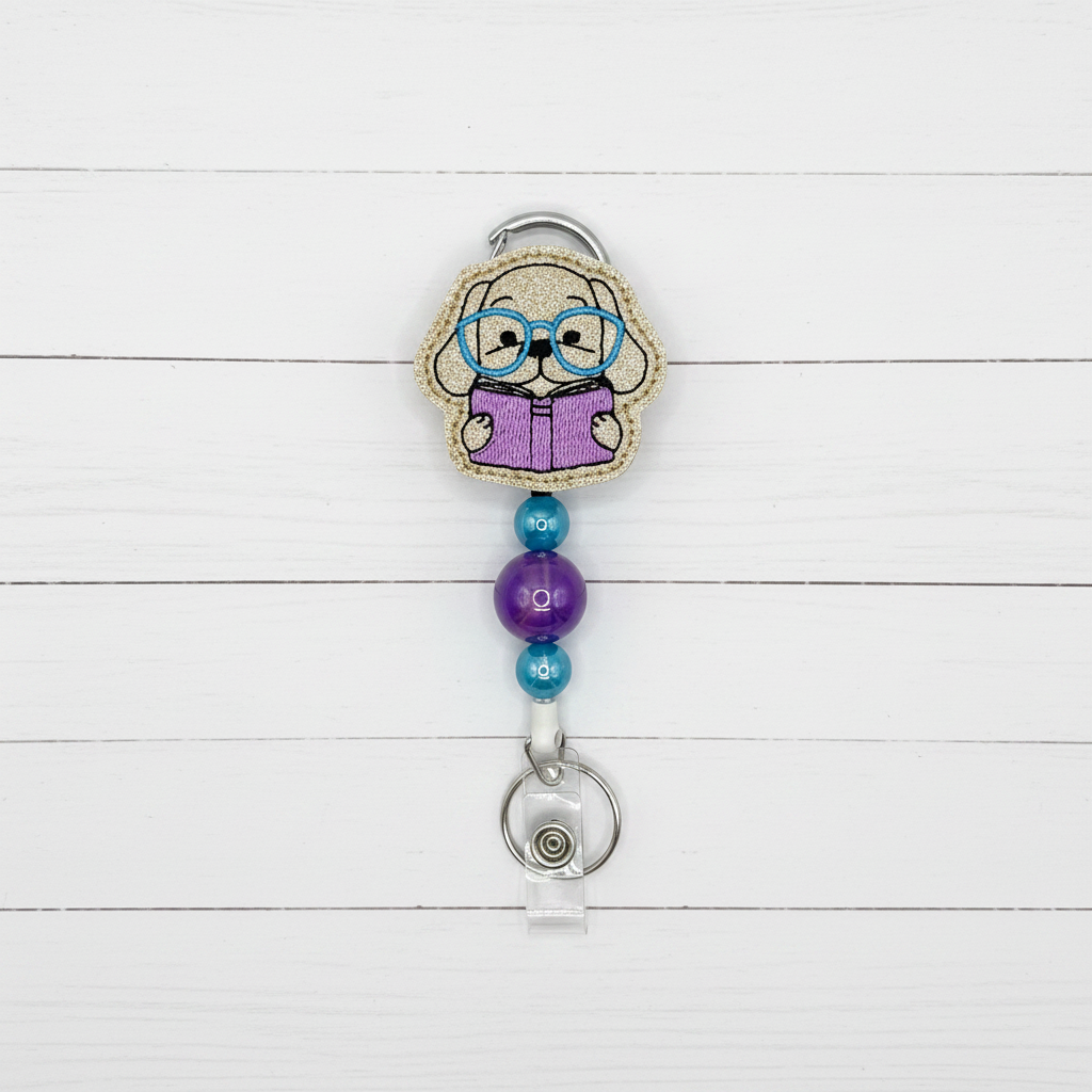 A novelty retractable badge reel featuring a cartoon elderly woman with glasses reading a purple book, attached to a silver metal clip and a clear plastic reel holder on a light lavender background.