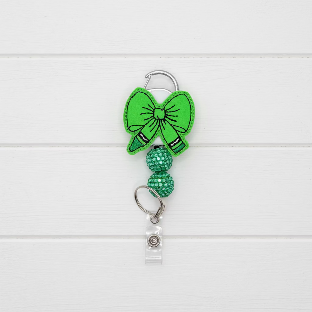 A bright green felt bow keychain accessory with a silver metal carabiner clip, a beaded green chain section, and a clear plastic badge holder at the bottom, shown on a light pink background.