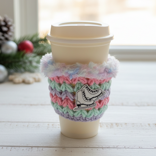 Coffee cup with a colorful crocheted sleeve featuring a snowflake design, placed on a wooden surface.