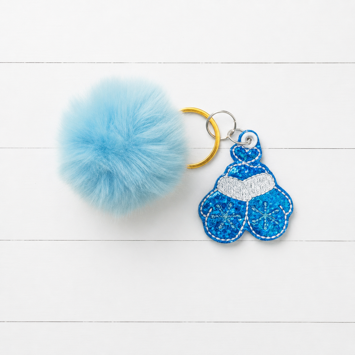 Blue Mitten Pom Pom Keychain on clean white painted wood background