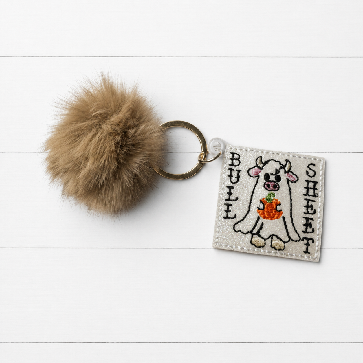 Bull Sheet Pom Pom Keychain on clean white painted wood background