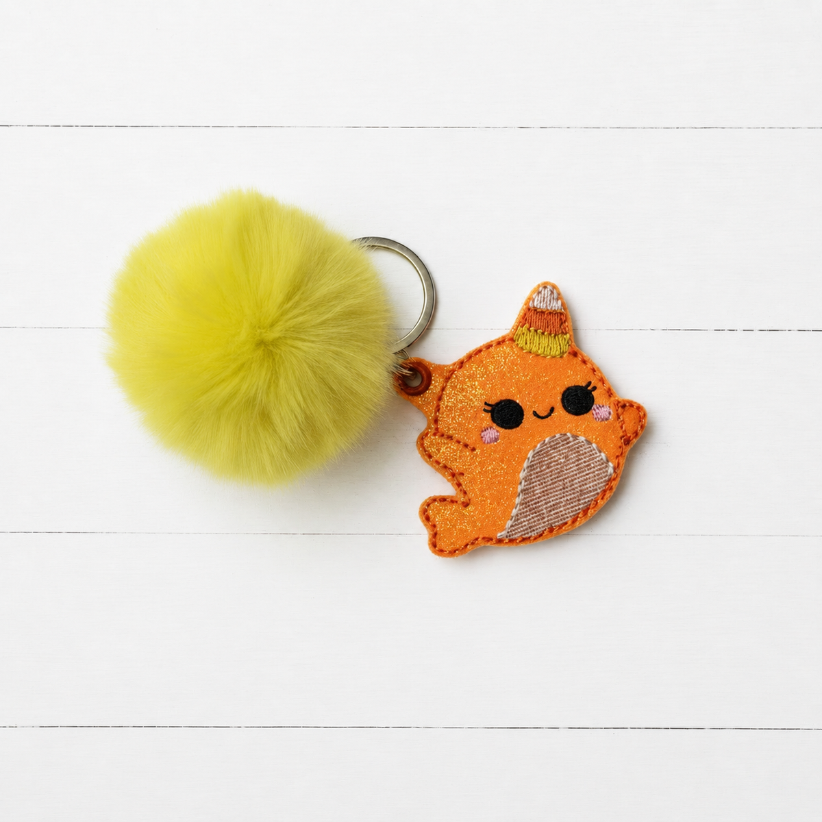 Candy Cane Narwal Pom Pom Keychain on clean white painted wood background