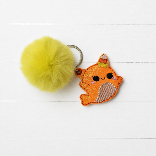 Candy Cane Narwal Pom Pom Keychain on clean white painted wood background