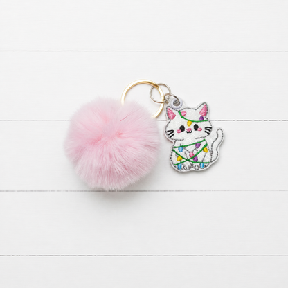 Christmas Light Kitten Pom Pom Keychain on clean white painted wood background